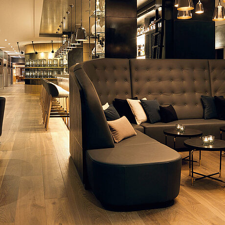 In der Lounge des Löwen Hotel Montafon ist eine gemütliche Sitzecke mit Rundtischen und Sesseln. Dahinter befindet sich die Hotelbar.